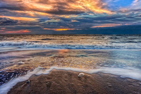 Zachód Słońca w chmurach na pięknej piaszczystej plaży z niebieskimi falami