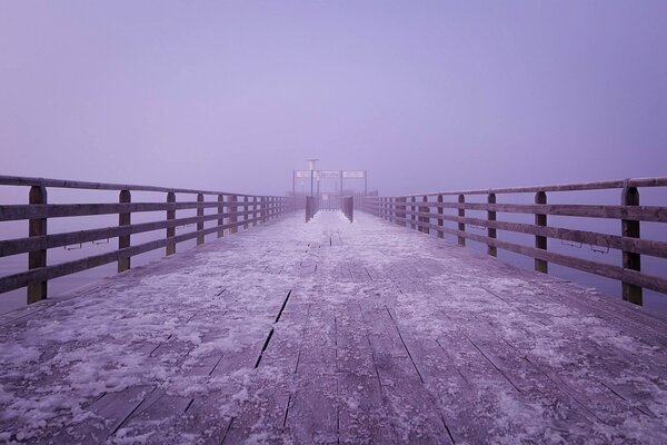 Nebbia lilla affondata su un ponte di legno coperto di neve