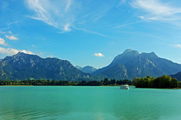 White yacht on the green surface of the river in Bavaria near the green mountains under a clear sky