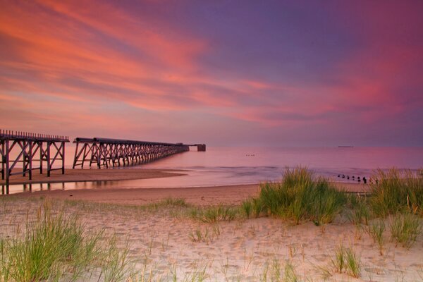 Puesta de sol en el mar con arena y muelle