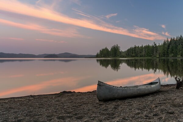 Лес отражается в воде и на берегу стоит лодка