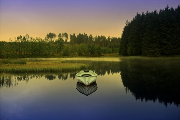 Reflection of a boat in the lake. Dawn in the forest