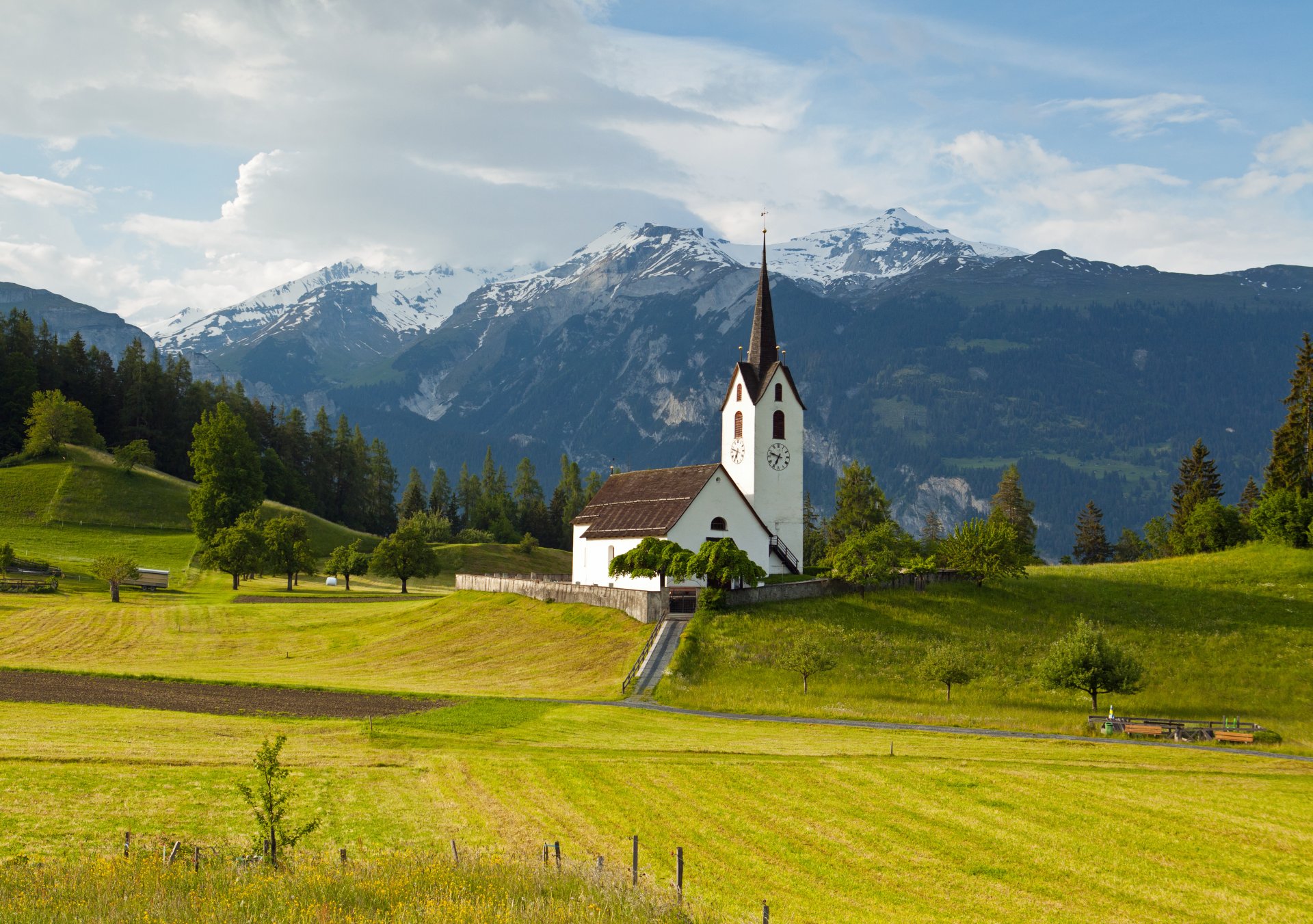 regine grigioni svizzera alpi montagne cime prato erba alberi chiesa cielo nuvole