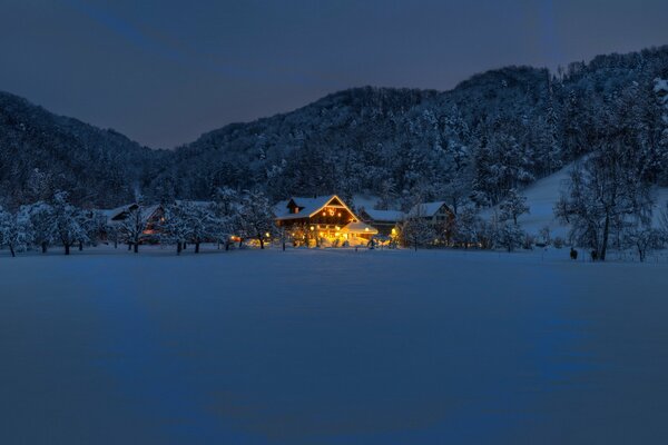 Casa en el bosque frente a las montañas en invierno en la nieve y las luces