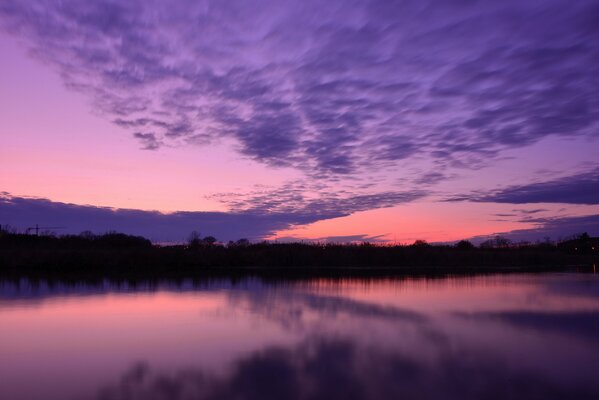 The smooth surface of the river and the distant forest against the background of the evening sky in purple-pink tones