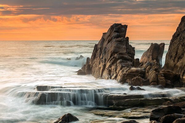 Scogliere sul mare contro il tramonto scarlatto