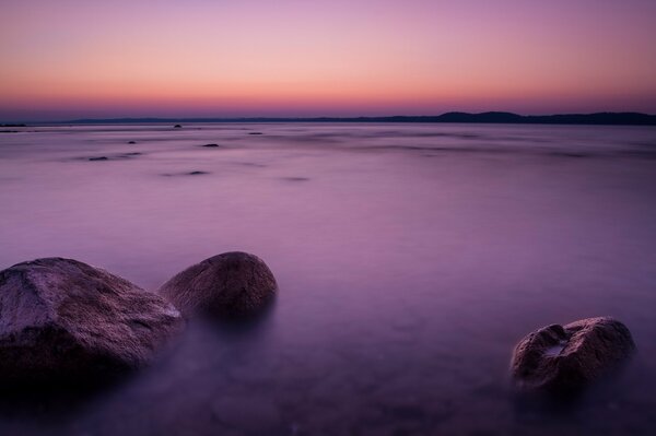 Puesta de sol lila sobre el mar con piedras