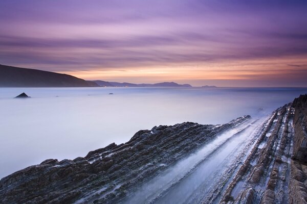 The rocky shore of the bay in Spain, against the background of an orange sunset