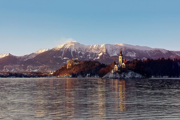 The castle surrounded by mountains and forest on the background of the water surface of the lake