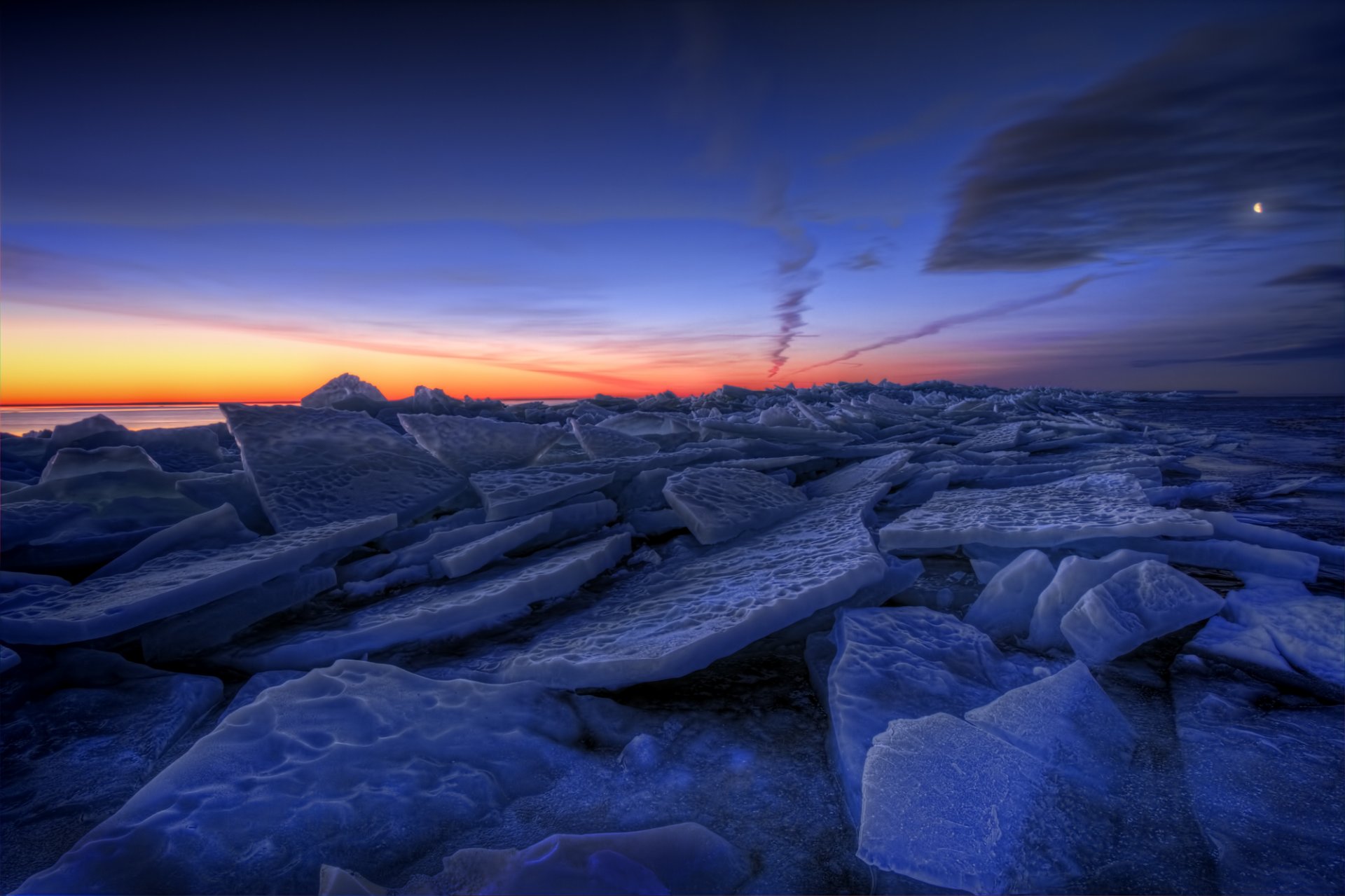 svezia inverno lago ghiaccio banchi di ghiaccio sera arancione tramonto blu cielo nuvole luna