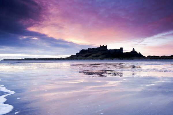 A lilac sunset is reflected in the sea against the background of the castle