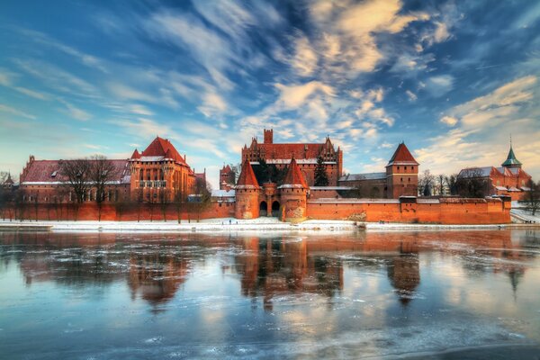 A castle in Poland in winter next to an ice lake in reflection