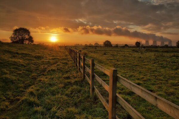 The setting sun over a field with a fence