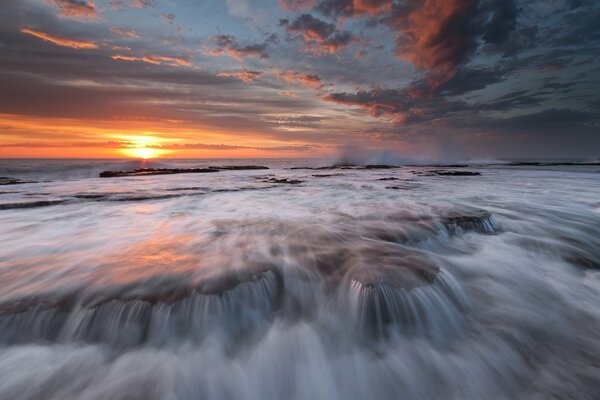 Ruisseaux de l eau bouillonnante de la mer au coucher du soleil