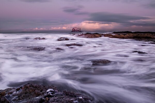 Bajo el cielo gris, las olas del mar ruedan sobre las rocas