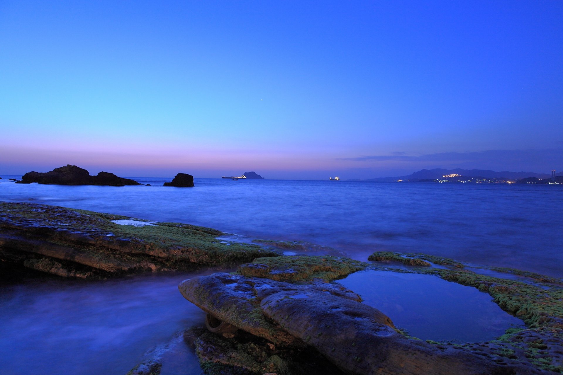 lila noche crepúsculo cielo azul nubes costa costa mar piedras musgo lejos ciudad luces