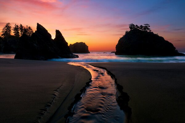 Romantic seascape - forest and rocks on the background of sunset reflected in the water