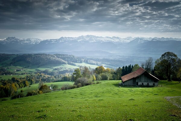 A house on a green hill. Mountains on the horizon