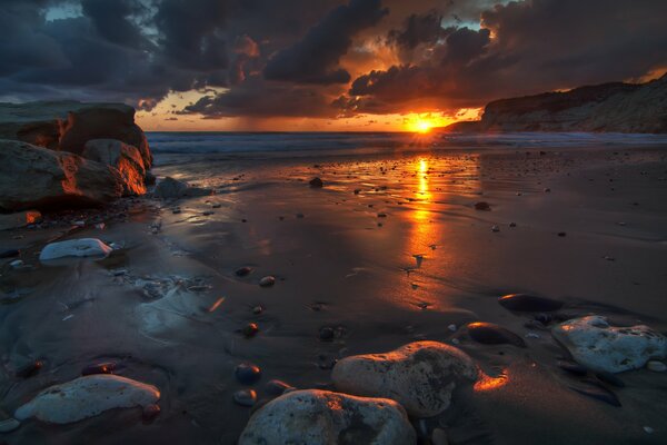 Темный пейзаж с морем камнями тучами и восходом солнца