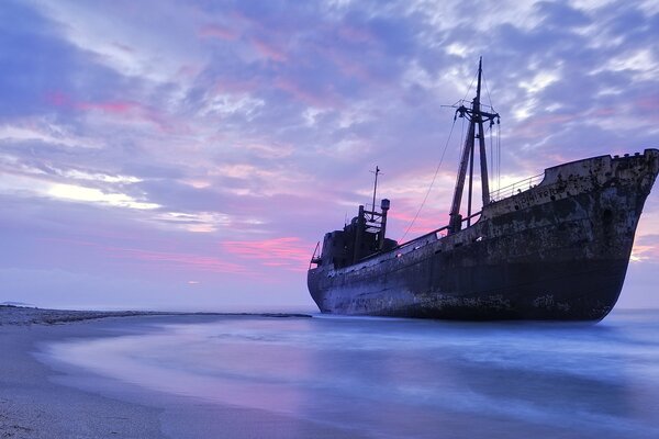 An old ship on a sandy beach at sunset