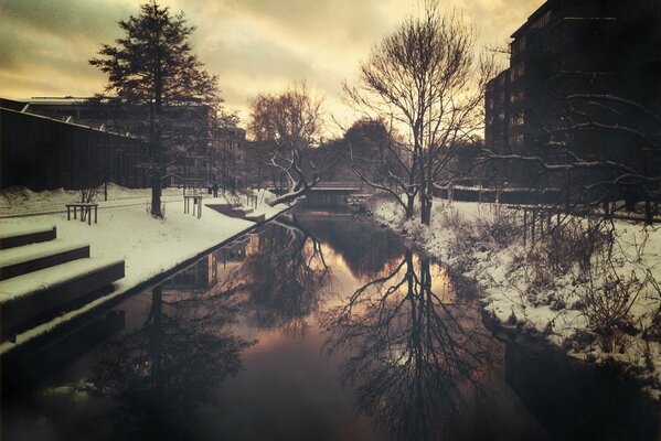 Verschneite Stadt am Abend. Brücke auf dem Wasser