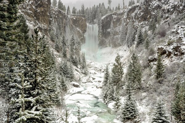 Ein Fluss mit einem Wasserfall entlang der schneebedeckten Klippen