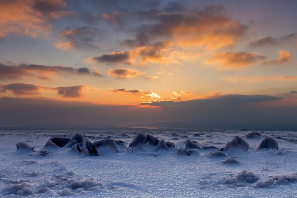 Stones covered with snow, against the background of the sunset sky