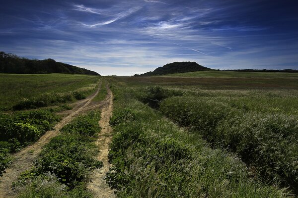 Una strada nel campo che conduce alle colline. Cielo blu