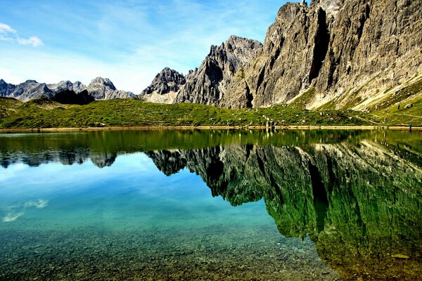 Die Wasseroberfläche des Sees spiegelt das Bergmassiv und das Grün wider