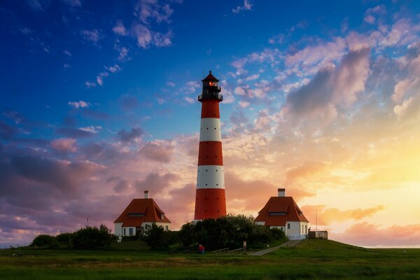 Lighthouse and houses on the background of a beautiful sunset sky