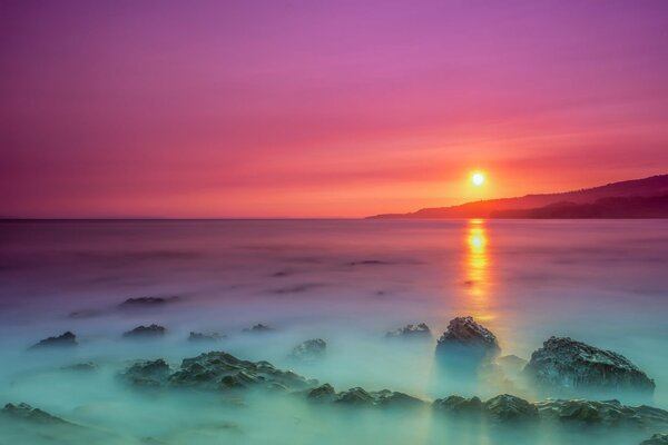 Amanecer sobre el océano con piedras