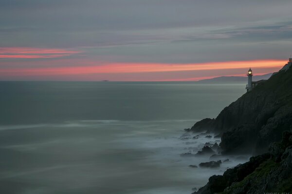 Phare au coucher du soleil. Roches et mer