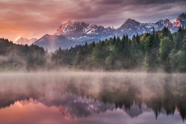 Niebla sobre el lago del bosque. Montañas en el fondo