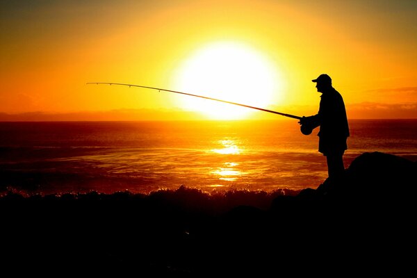La silueta de un pescador en el fondo de la puesta de sol del mar