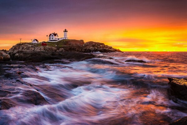 Morgendämmerung am Meer. Ein Leuchtturm steht auf den Felsen