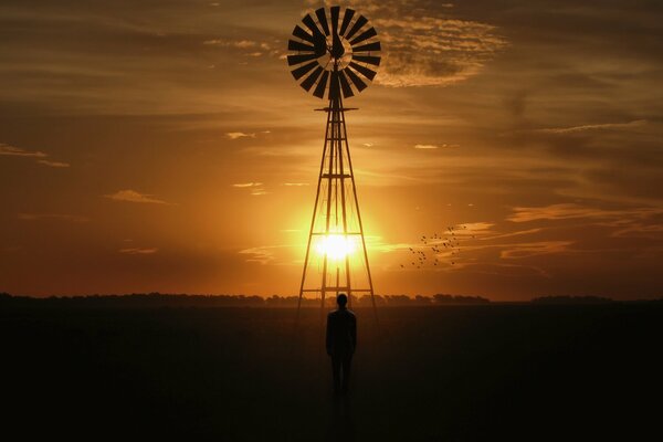 A man and a windmill on the background of the sunset sky