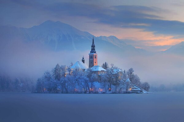 Eslovenia. Una iglesia cubierta de nieve en medio de un campo cubierto de nieve. Sobre ella la niebla