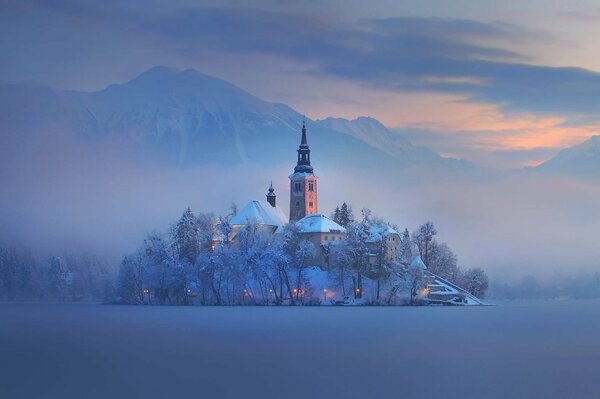 Slovénie. Église couverte de neige, au milieu d un champ enneigé. Au-dessus de son brouillard
