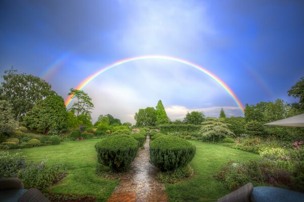 Regenbogen am Himmel vor dem Hintergrund des grünen Waldes, die Straße führt zum Regenbogen