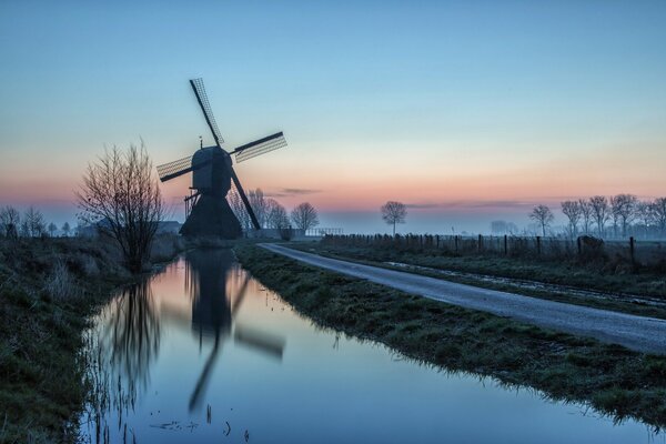 Windmühle und Straße am Wasser, im Hintergrund des Sonnenuntergangs