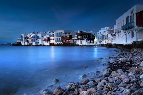 Casas griegas de juguete brillan con un resplandor lunar en la costa rocosa del mar