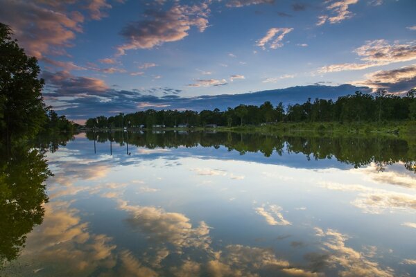 A water surface with a reflection of the sky. Evening. Reflection of clouds in the water. Forest on the shore