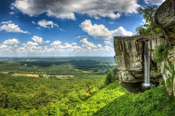 High cliffs. Waterfall of rocks. Green valley and blue sky with white clouds