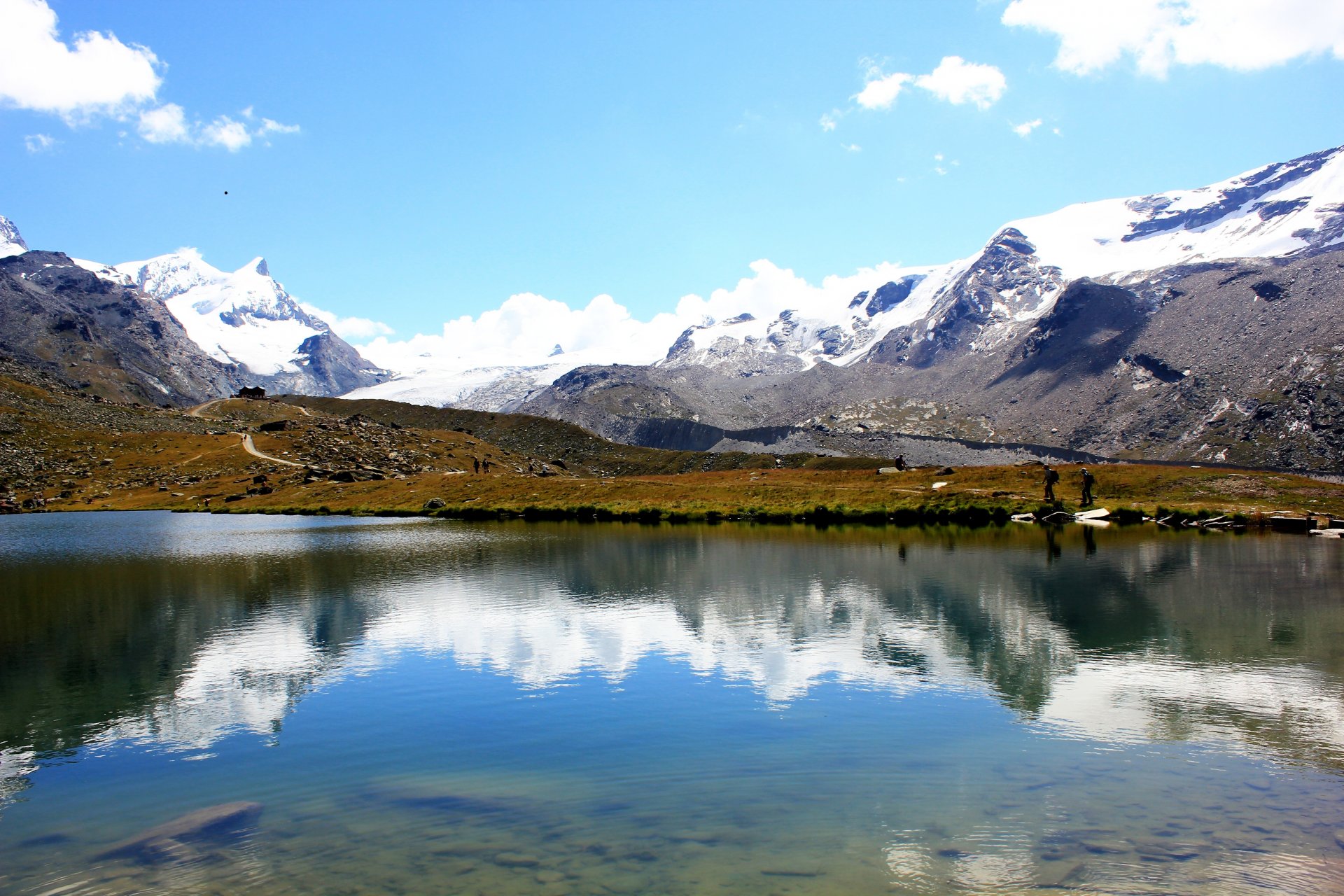 montañas picos nieve lago reflexión carretera gente cielo nubes