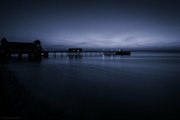 Calm night sea. Pier with lights at dusk