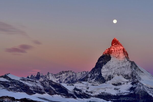 Der Gipfel der Alpen vor dem Hintergrund des zwielichtigen Himmels. Mond über dem Gipfel