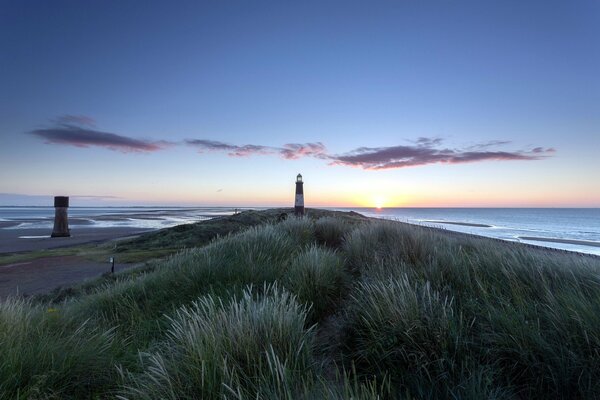 Faro solitario al tramonto vicino al bordo dell acqua