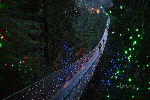 La gente cruza el puente colgante con luces navideñas