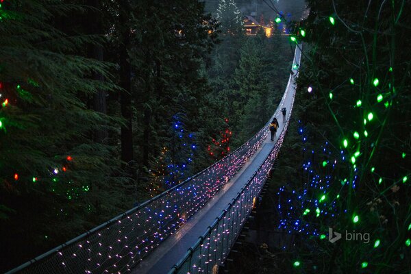 Люди переходят висячий мост с праздничными огнями