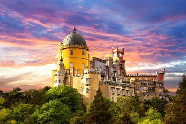 Palais noyé dans la verdure sur fond de ciel coucher de soleil bleu et rose